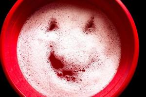 bacia de plástico vermelha com um rosto emoji na superfície da água. espuma branca com rosto sorridente. foto