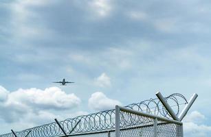 avião voando no céu azul e nuvens brancas acima da cerca de metal. negócios de aviação. avião comercial. transporte aéreo. cerca para segurança e proteção. negócios de aviação. viajar de avião. foto