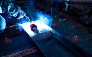 soldador de solda de metal com máquina de solda a arco de argônio e tem faíscas de soldagem. um homem usa luvas de proteção. segurança no trabalho industrial. soldador trabalhando com segurança. trabalhador na fábrica da indústria siderúrgica. foto