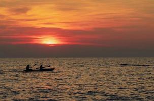 silhueta de casais estão andando de caiaque no mar ao pôr do sol. caiaque no mar tropical ao pôr do sol. casal romântico viaja nas férias de verão. atividades de aventura de casais românticos. lindo céu por do sol foto