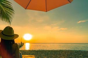 sexy, aproveite e relaxe a mulher usar biquíni deitado e tomando sol na espreguiçadeira na praia de areia na ilha tropical paradisíaca sob o guarda-sol ao pôr do sol. férias de verão. viagens de férias. Ritmo de verão. foto