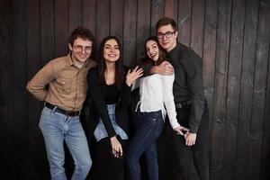 quatro funcionários têm uma pausa. juventude fica contra a parede de madeira preta. grupo de amigos passando tempo juntos foto