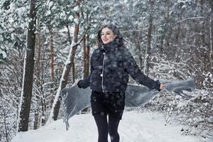 correndo para a frente. retrato de mulher encantadora na jaqueta preta e cachecol cinza na floresta de inverno foto