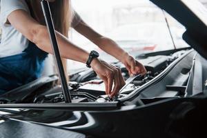 colocação da bateria. no lindo trabalho. mulher viciada em carro repara automóvel preto dentro de casa foto