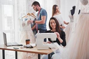 trabalho está em andamento. estilista feminina trabalha nas novas roupas na oficina com grupo de pessoas atrás foto