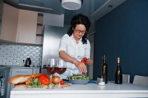 ela sabe o que fazer. mulher de camisa branca preparando comida na cozinha usando legumes foto