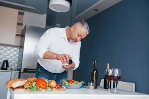 será delicioso. homem de camisa branca preparando comida na cozinha usando legumes foto