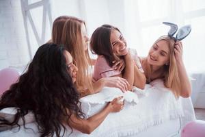 sorrisos fofos. meninas alegres de pijamas deitadas na cama no quarto branco e celebram foto