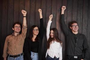 união das pessoas. comemorando o sucesso. amigos colocam as mãos contra a parede de madeira preta foto