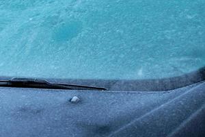 closeup vista frontal do carro estacionado no estacionamento ao ar livre que pára-brisa e capô coberto por chuva congelante e pequena pelota de gelo. conceito de mudança climática. aviso do ambiente. textura de pellet de gelo foto