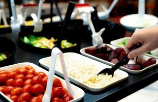 mão segurando a colher para colher as lágrimas do trabalho cozido no bar de saladas. buffet de saladas no restaurante. buffet de saladas para almoço ou jantar. comida saudável. restauração de alimentos. serviço de banquete. comida vegetariana. foto