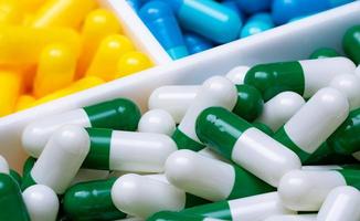 foco seletivo em comprimidos de cápsula verde-brancos em caixa de plástico em comprimidos de cápsula azul e amarelo turva. indústria farmacêutica. produtos de farmácia. fundo para o negócio de seguro de saúde.