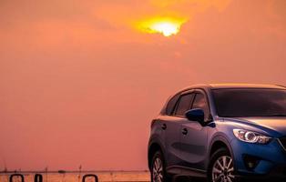 carro suv compacto azul com esporte e design moderno estacionado na estrada de concreto à beira-mar ao pôr do sol à noite. conceito de tecnologia de carro híbrido e elétrico. indústria automobilística. viagem de viagem. foto