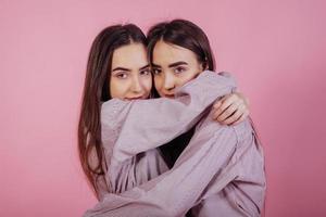 abraços fofos. duas irmãs gêmeas em pé e posando no estúdio com fundo branco foto