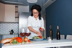 vista frontal. mulher de camisa branca preparando comida na cozinha usando legumes foto