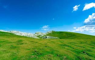 paisagem de grama verde e colina de pedra na primavera com lindo céu azul e nuvens brancas. campo ou vista rural. fundo da natureza em dia ensolarado. ambiente de ar fresco. pedra na montanha.