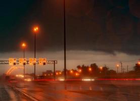 luz de rua à noite em dia chuvoso. carro e caminhão na estrada de asfalto. noite escura na estrada com luz de lâmpada elétrica e sinal de tráfego de limite de velocidade e símbolos de velocidade da câmera. luz de rua vermelha e céu escuro. foto