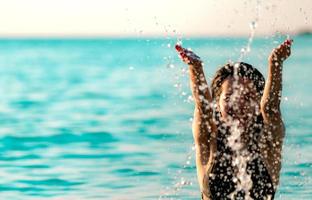 feliz jovem asiática em maiô preto relaxe e aproveite as férias na praia do paraíso tropical. garota em férias de verão espirrar água no mar. modelo sexy. mulher sexy de biquíni preto. Ritmo de verão. foto