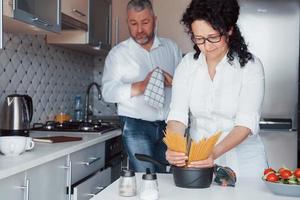 colocando espaguete para o preparo. homem e sua esposa de camisa branca foto