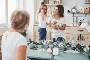 biscoito perto do olho do garoto. mãe, avó e filha se divertindo na cozinha foto