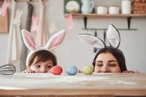 olha para os ovos. mãe e filha em orelhas de coelho na páscoa se divertem na cozinha durante o dia