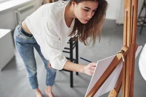 designer trabalha em seu estúdio de arte. jovem morena na sala com paredes brancas e luz do dia que vem da janela foto