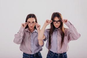 testa novos óculos. duas irmãs gêmeas em pé e posando no estúdio com fundo branco foto