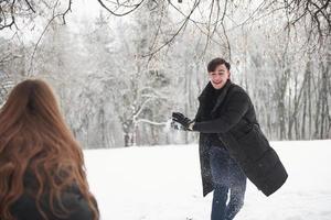 namorado corre para a frente. lindo casal jovem jogando e jogando bolas de neve na floresta de inverno foto