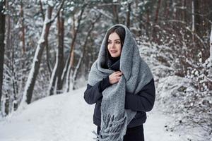 o inverno é encantador. retrato de mulher encantadora na jaqueta preta e cachecol cinza na floresta fria de neve foto