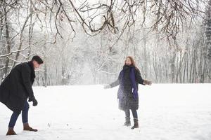 vamos relembrar nossa infância. lindo casal jovem jogando e jogando bolas de neve na floresta de inverno foto