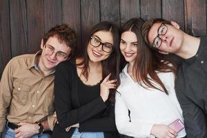 inclinando-se um para o outro. juventude fica contra a parede de madeira preta. grupo de amigos passando tempo juntos foto