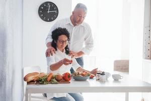 vamos comer isso. homem e sua esposa de camisa branca preparando comida na cozinha usando legumes foto