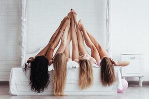 tocando um ao outro. quatro mulheres jovens com boa forma corporal, deitadas na cama com as pernas para cima foto