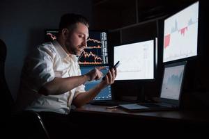 ligando para o parceiro de negócios. homem barbudo de camisa branca trabalha no escritório com várias telas de computador em gráficos de índice foto