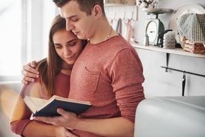 abraça um ao outro. casal fofo lendo livro juntos em casa na cozinha durante o dia foto