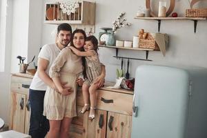 foto de família fofa de mãe grávida, pai e filha. de pé na cozinha