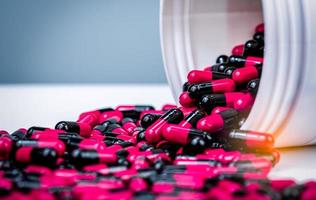 pílula de cápsulas pretas e rosa derramadas do recipiente de garrafa de plástico branco. medicamento prescrito. resistência a antibióticos. pílulas cápsula antimicrobiana. indústria farmacêutica. fundo de farmácia. foto