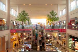 fundo de shopping turva. pessoas andando e fazendo compras nas férias. pessoas em escadas rolantes no moderno shopping center naquele segundo andar decorado com duas árvores para um ambiente fresco. foto