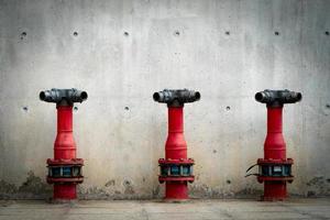 três bombas de segurança contra incêndio no piso de cimento do edifício de concreto. sistema de dilúvio do sistema de combate a incêndios. encanamento de proteção contra incêndio. bomba de incêndio vermelha na frente da parede de concreto. bomba de segurança contra incêndio de alta pressão. foto