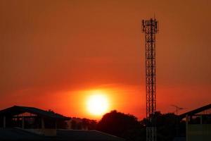 lindo céu pôr do sol vermelho e laranja. torre de telecomunicações silhueta à noite com lindo céu vermelho pôr do sol e nuvens. fundo da natureza. céu vermelho do sol no verão. céu de verão tropical. foto