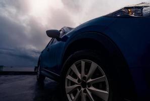 novo carro suv azul de luxo estacionado na estrada de concreto ao lado da praia em dia chuvoso com céu tempestuoso. vista frontal do carro suv azul com design esportivo. gotas de chuva no carro. viagem de viagem. dirigir com mau tempo. foto