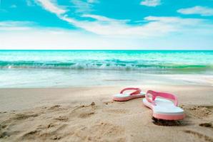 sandálias rosa e brancas na praia de areia. flipflop estilo casual foram removidos à beira-mar. férias de verão na praia tropical. divertidas viagens de férias na praia. horário de verão. Ritmo de verão. tempo relaxante. foto