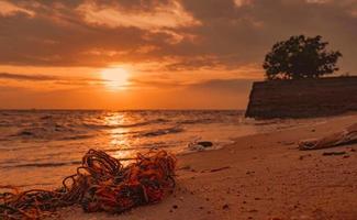 lixo na praia. poluição ambiental costeira. problemas ambientais marinhos. corda velha na praia de areia na hora do sol, perto da costa do mar. lixo na praia tropical afeta a saúde mental do turista. foto