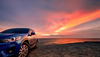 carro suv compacto azul com design esportivo e moderno estacionado na praia ao pôr do sol. tecnologia de carros híbridos e elétricos. vaga de estacionamento. indústria automobilística. fundo de negócios de cuidados de carro. céu bonito. foto