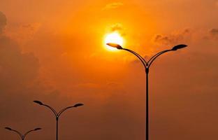 poste elétrico de rua silhueta com lindo céu pôr do sol laranja e amarelo e nuvens à noite. luz da lâmpada de rua. poste de luz da estrada da cidade para o conceito de energia e conservação de energia de iluminação. foto