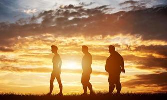 três silhuetas de homens com diferentes tipos de corpo em um céu pôr do sol foto