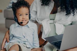 feliz menino afro-americano conversando com a família através da webcam no laptop com a ajuda das mães foto