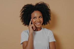 mulher africana pensativa com cabelo encaracolado tocando o templo com o dedo indicador, isolado em fundo bege foto