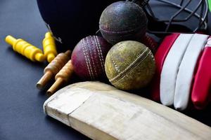 equipamentos de esporte de críquete de treinamento antigo no chão escuro, bola de couro, postigos, capacete e taco de madeira, foco suave e seletivo, amantes do esporte de críquete tradicional em todo o conceito do mundo. foto