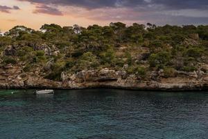 veleiro movendo-se por penhasco rochoso no mar Mediterrâneo na ilha durante o pôr do sol foto